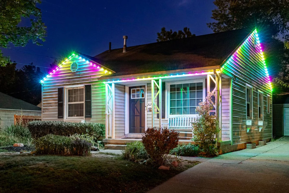 3L light landing page photos (1) A single-story house in New Franklin at night features colorful holiday lighting outlining the roof and porch, illuminating the beige siding and front yard with shrubs and a walkway.