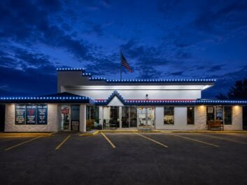 2 A diner with blue string lights and an American flag on the roof, photographed at dusk. The parking lot is empty and the sky is dark blue with clouds.